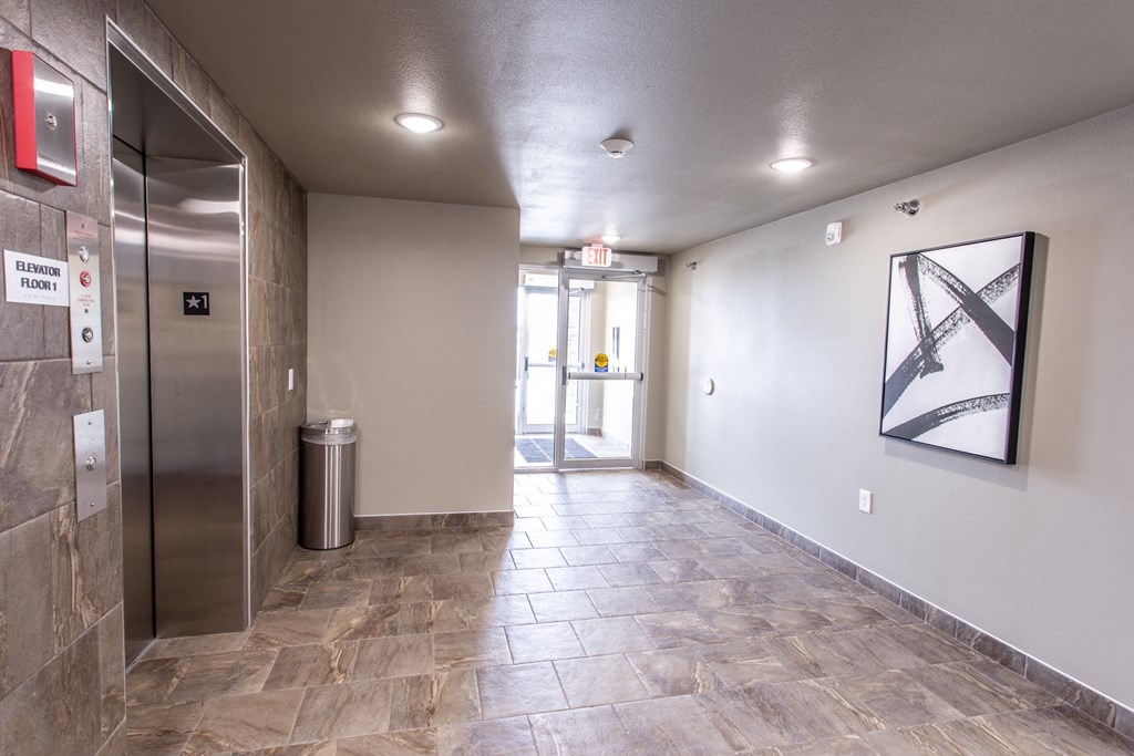 an empty hallway with a stainless steel elevator and a painting on the wall