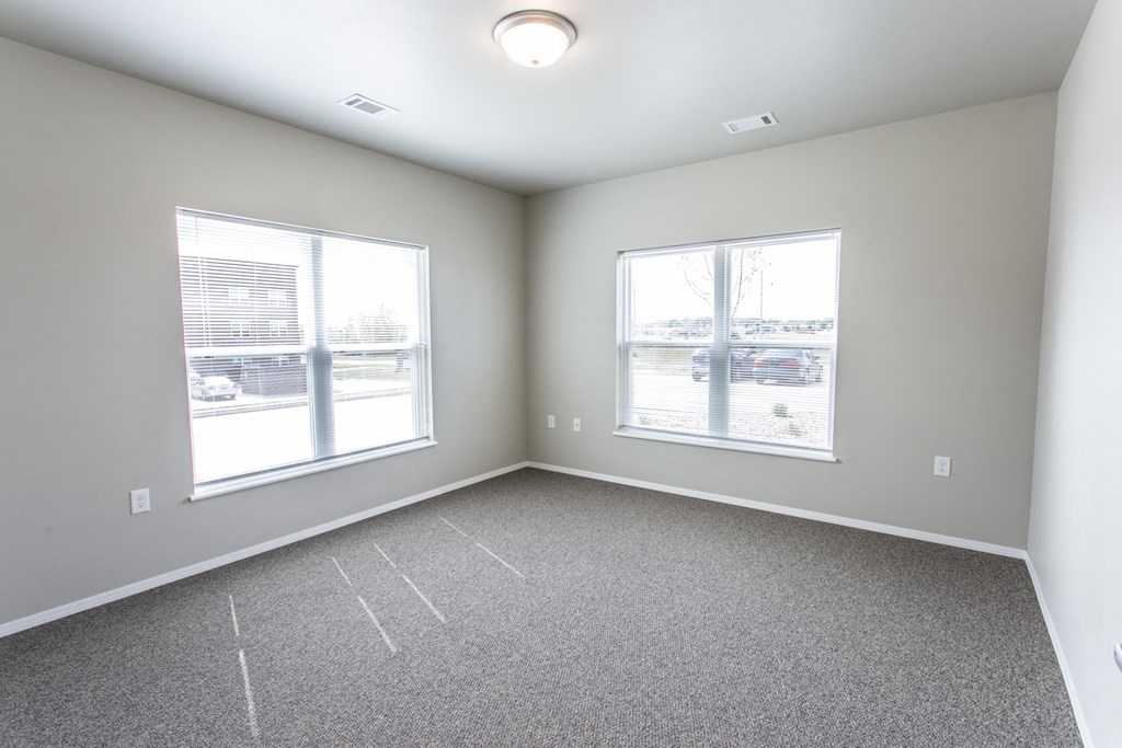 an empty room with two windows and carpeting