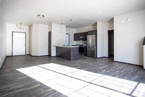 an empty living room with a kitchen with stainless steel appliances