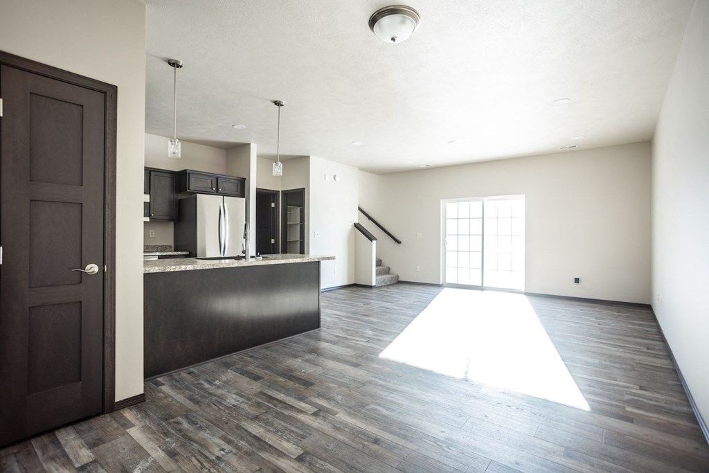 an empty living room with a kitchen and a door