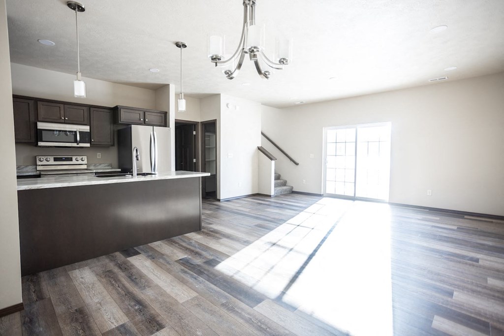an empty living room with a kitchen and a chandelier