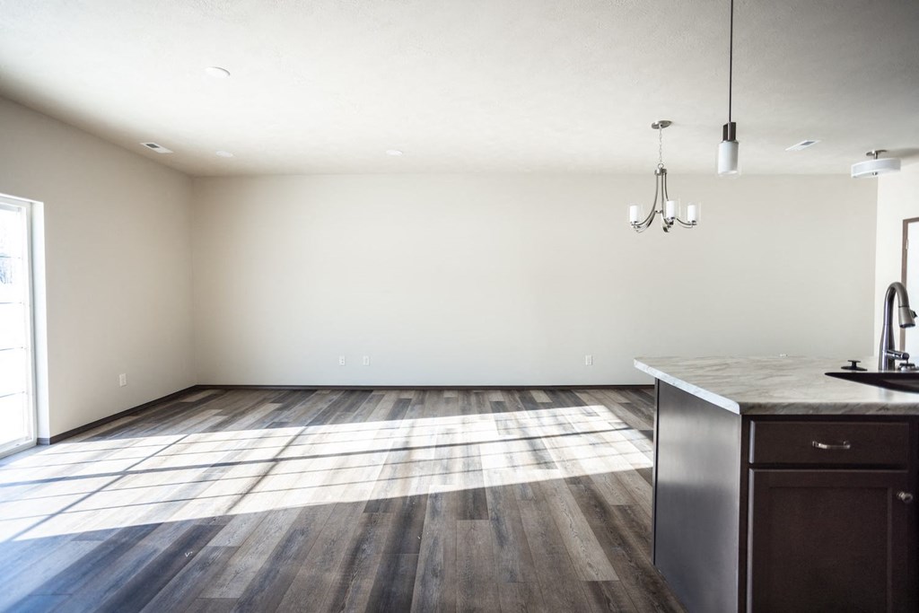 an empty living room with wood floors and a kitchen