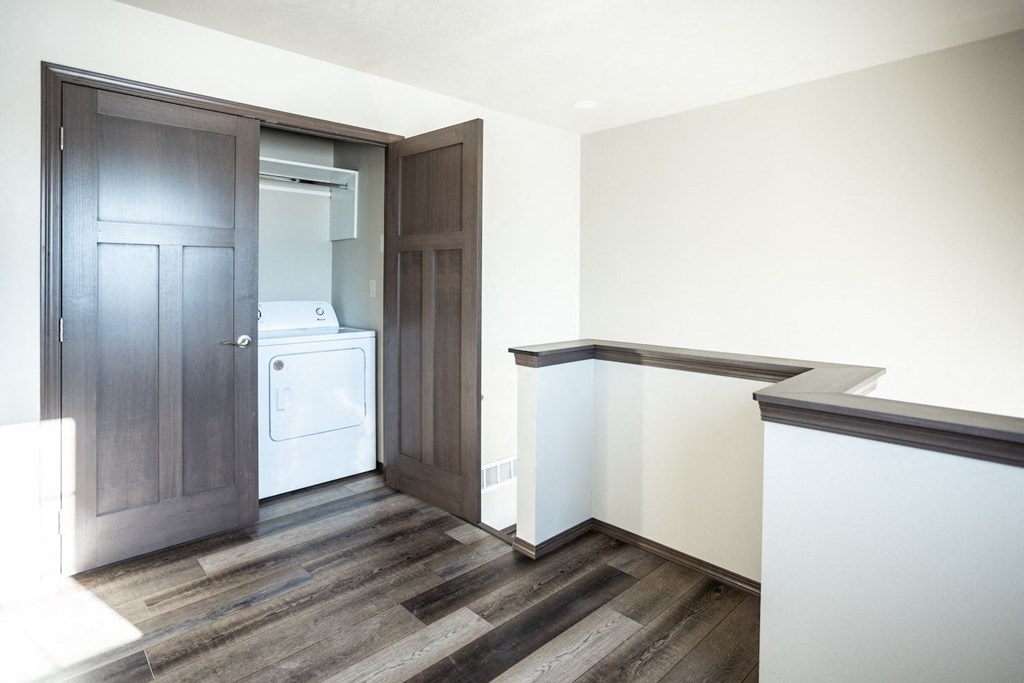 a laundry room with a washer and dryer and white walls and wood floors