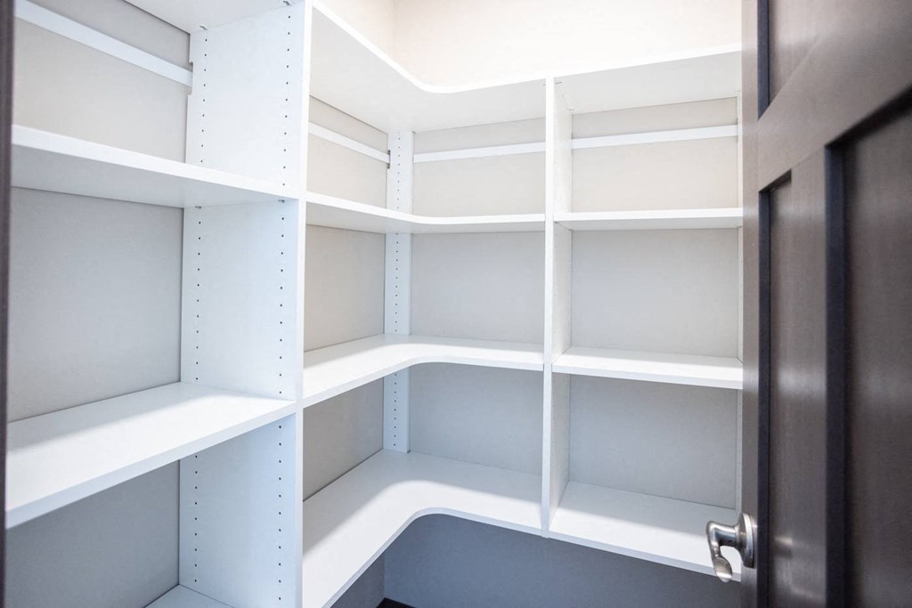 a walk in closet with white shelves and a door