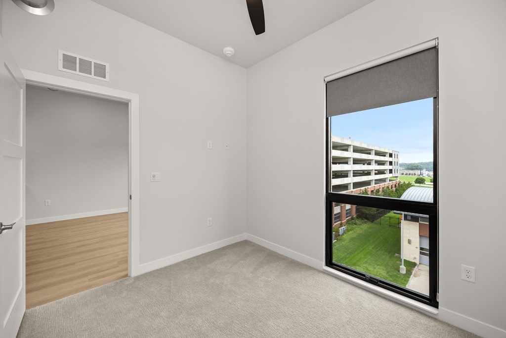 A room with a window that has a view of a building and a lawn outside.