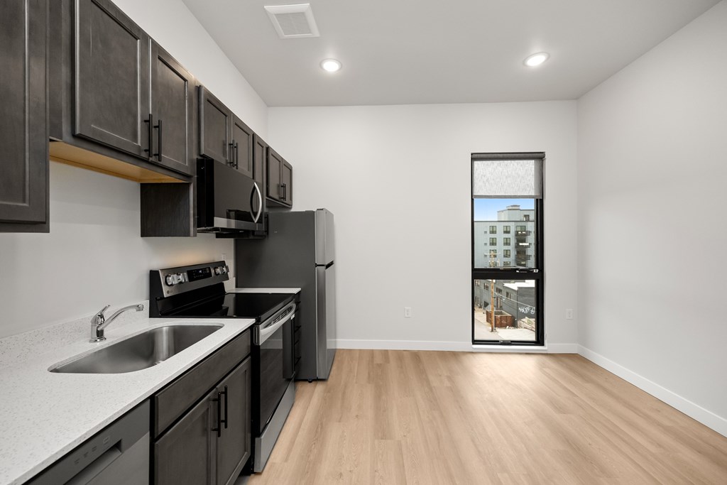 A kitchen with black cabinets and a window showing a building.