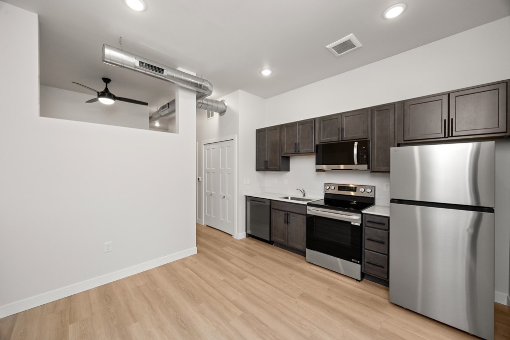 A modern kitchen with a stainless steel refrigerator and wooden flooring.