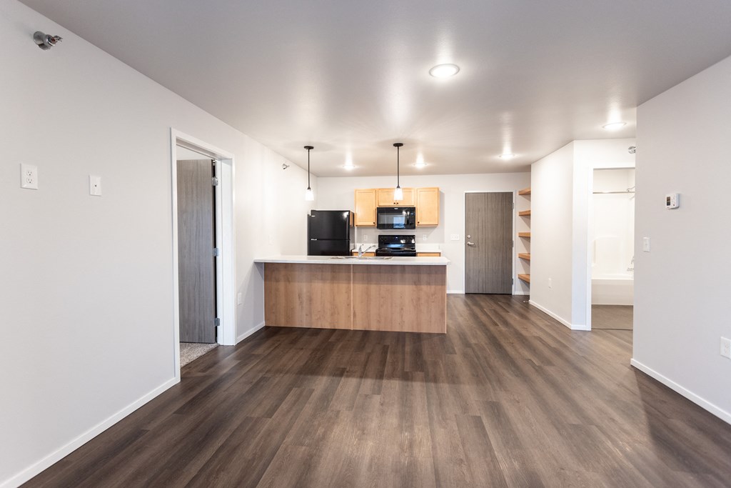 an empty living room and kitchen with wood floors and white walls