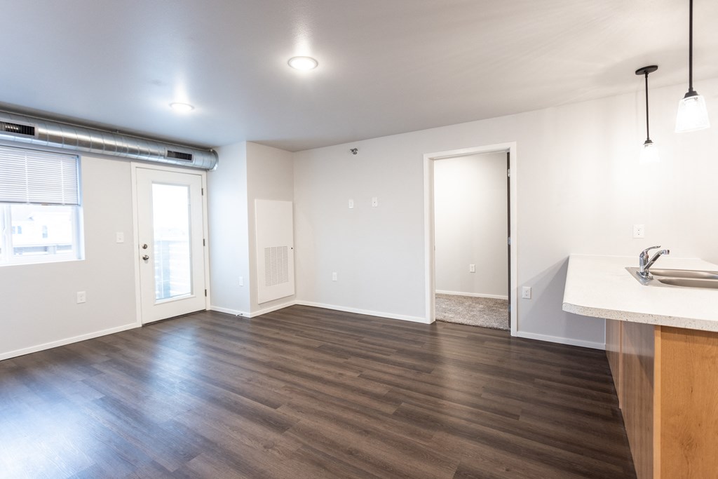 an empty living room with wood flooring and a kitchen