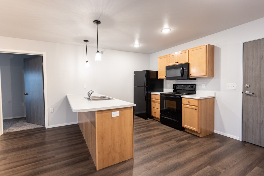 an empty kitchen with wood flooring and a black refrigerator