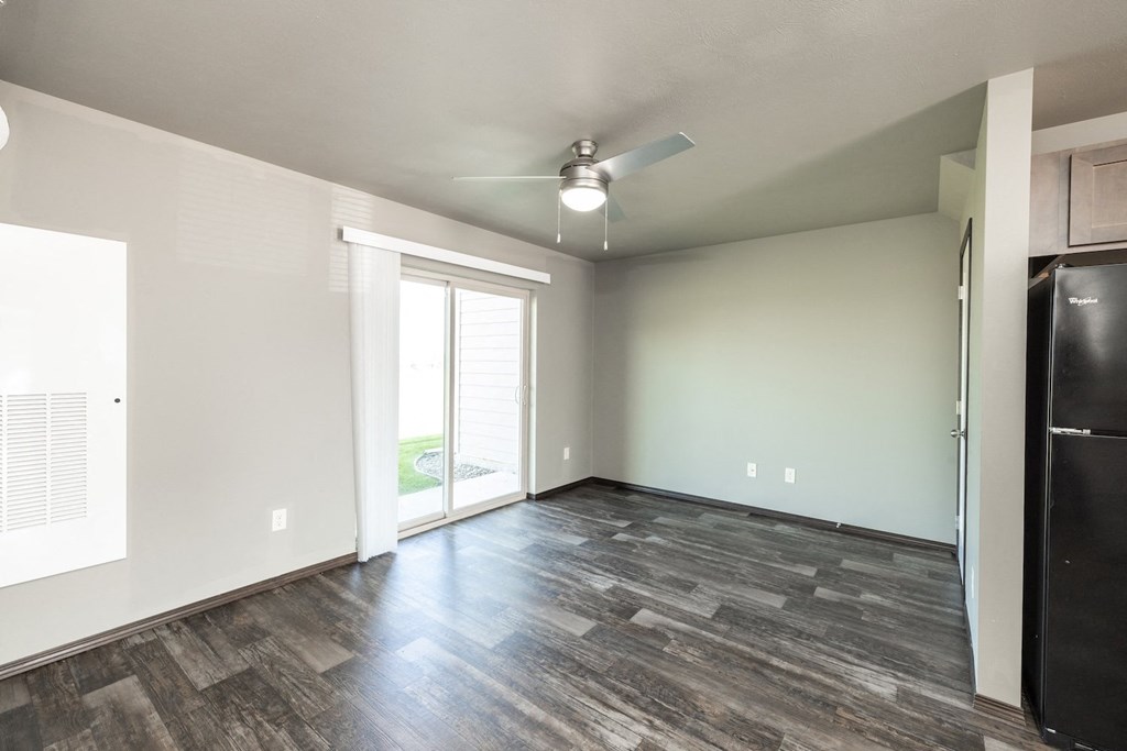 an empty living room with a refrigerator and a ceiling fan