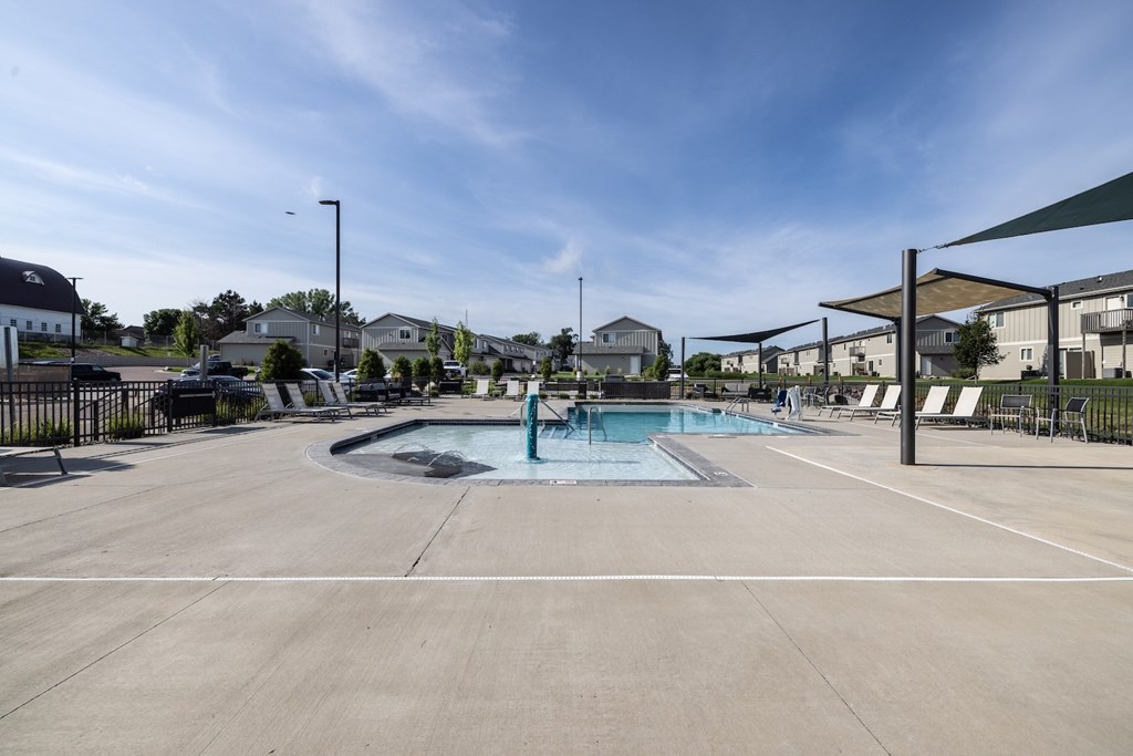 A large outdoor swimming pool with a hot tub and lounge chairs.