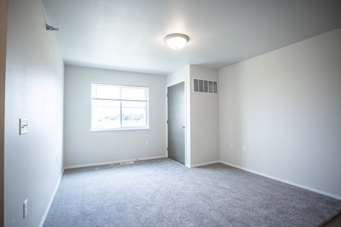 A spacious room with a window and carpeted floor.