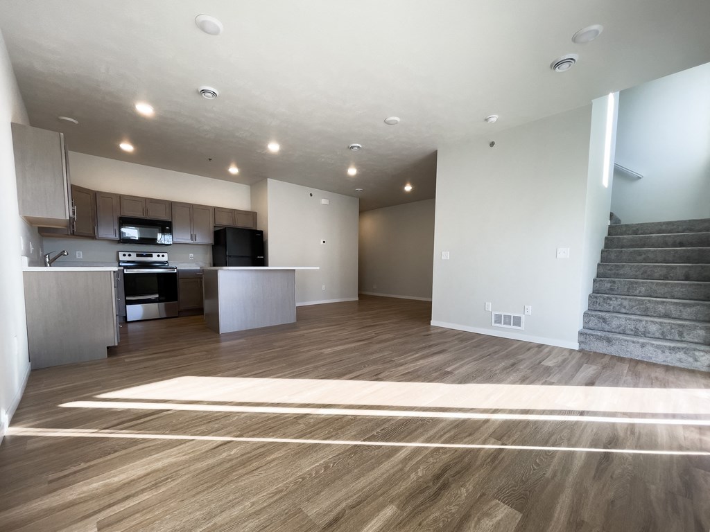an empty living room with a kitchen and stairs