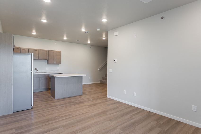 an empty living room with a kitchen and a refrigerator