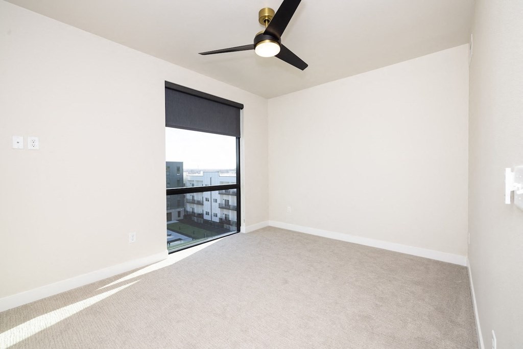 A room with a ceiling fan and a window overlooking a building.