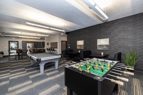 A foosball table is in the middle of a room with a pool table and a ping pong table.