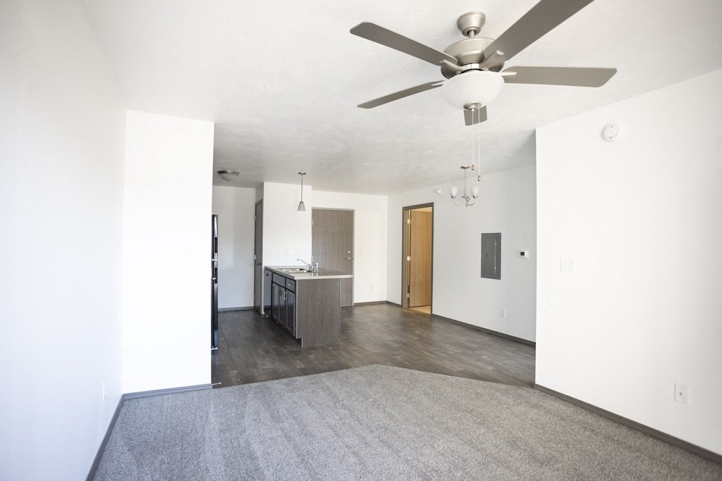 an empty living room with a ceiling fan and a kitchen