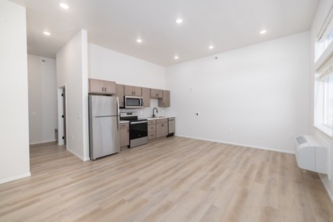 A kitchen with white walls and wooden floors with a refrigerator, microwave, oven, and sink.