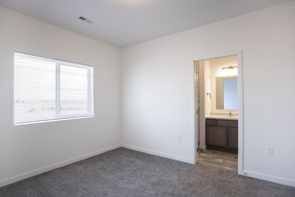 an empty bedroom with a window and a bathroom