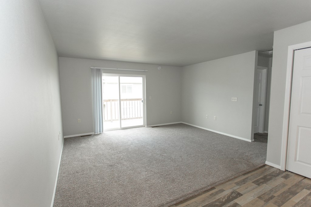 an empty living room with white carpet and a door to a balcony
