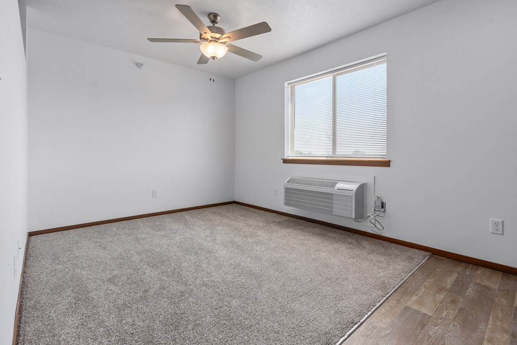 A room with a ceiling fan, carpeted floor, and a window with blinds.