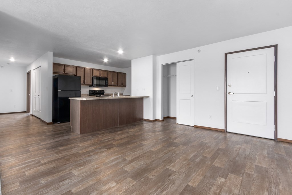 A kitchen with a black fridge and microwave, brown cabinets, and a wooden floor.