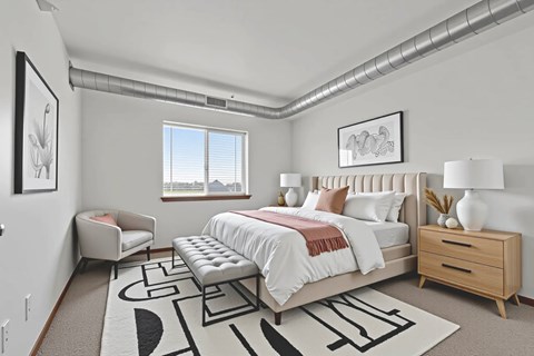 A bedroom with a large bed, a bench, and a rug with a black and white design.