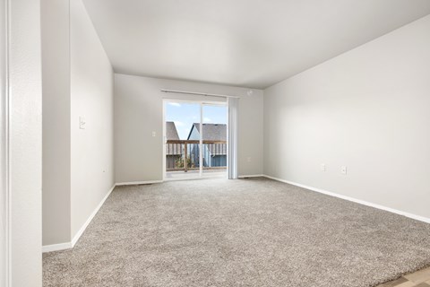 A spacious room with a carpeted floor and a sliding glass door leading to a balcony.