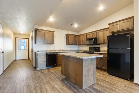 A kitchen with a black refrigerator and wooden cabinets.