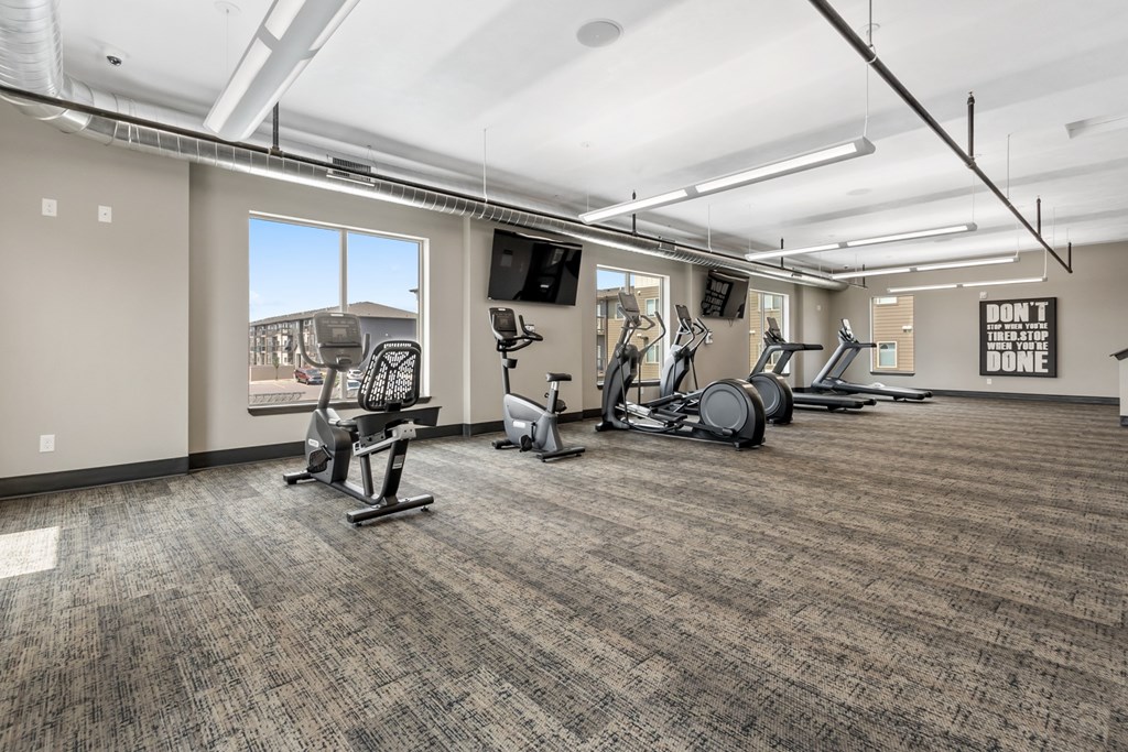 A gym with a variety of exercise equipment and a motivational poster on the wall.