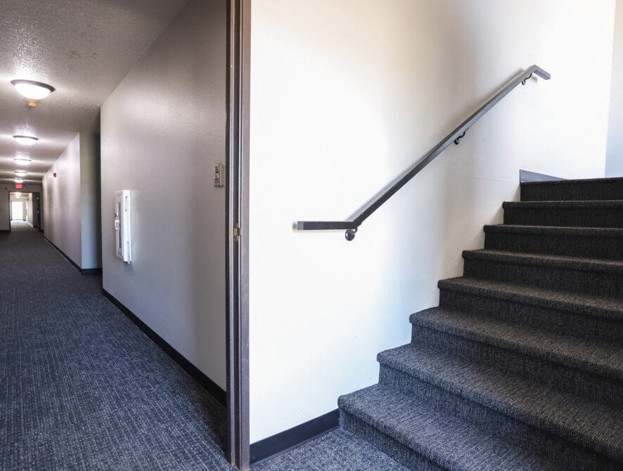 a hallway with stairs and a railing next to a white wall