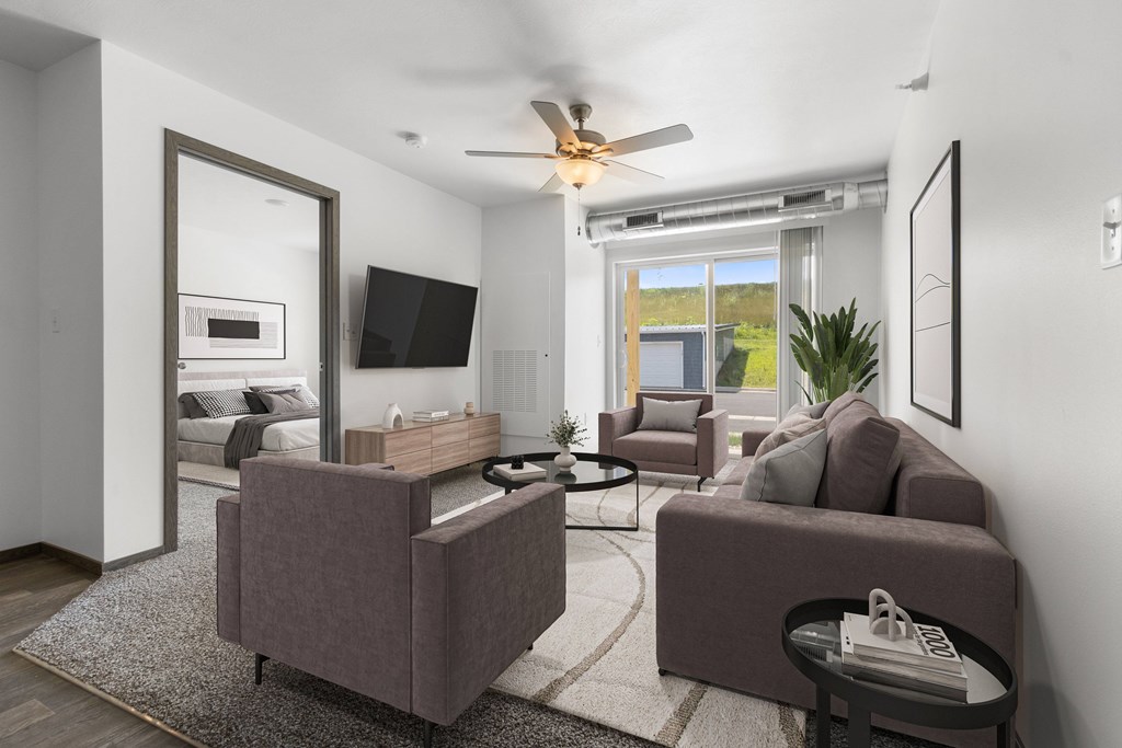 A living room with a brown couch, a grey couch, a television, and a ceiling fan.