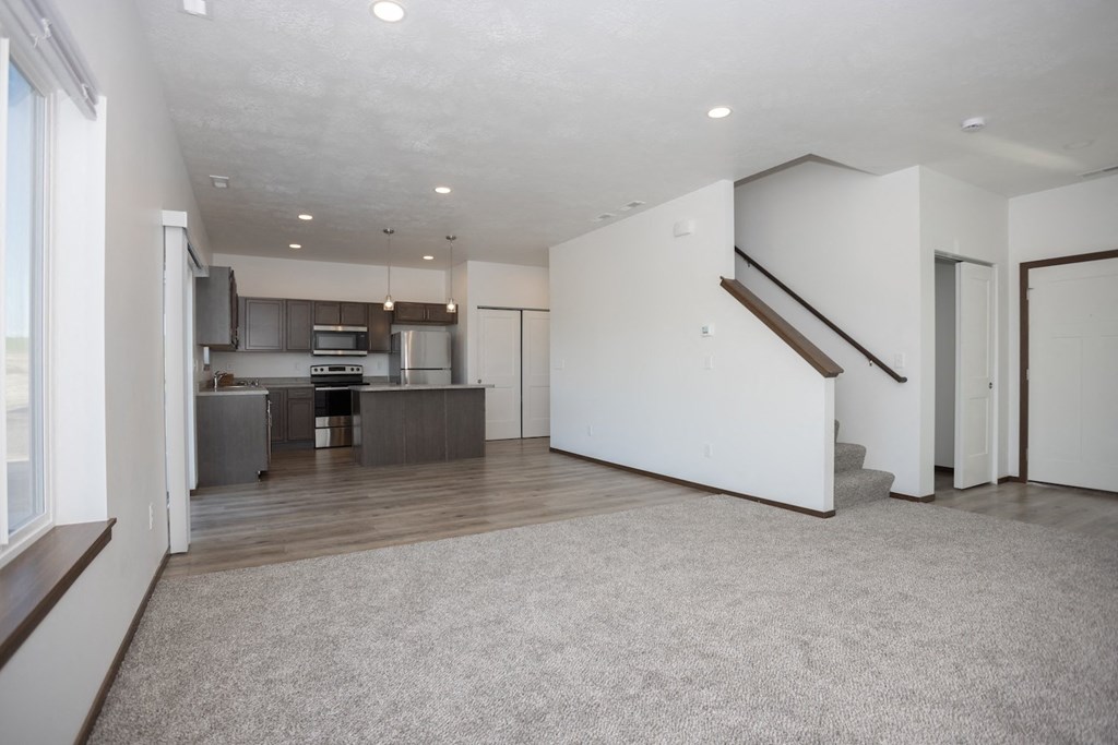 the living room and kitchen of an empty house with white walls and wood flooring