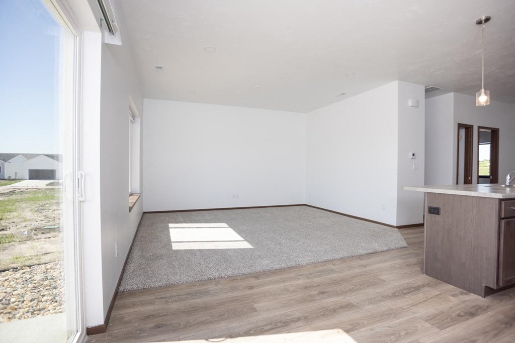 an empty living room with a kitchen and a window