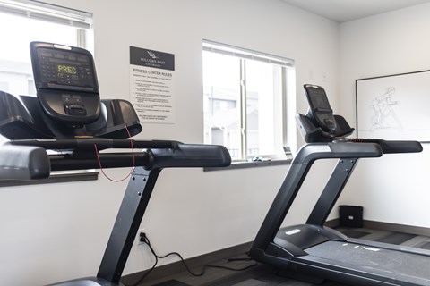 Two treadmills are in a gym with a sign that says "Fitness Center Rates.".