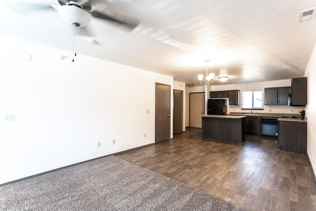 an empty living room with a kitchen and a ceiling fan