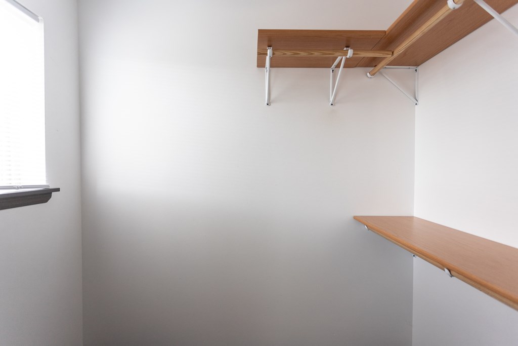 a walk in closet with a wooden shelf and a white wall