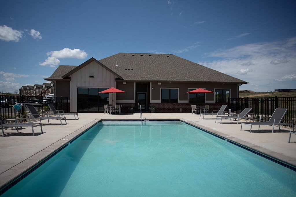 a swimming pool with chairs and a building in the background