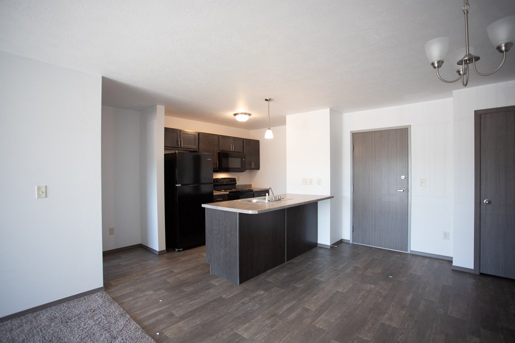 an empty apartment with a kitchen and a black refrigerator