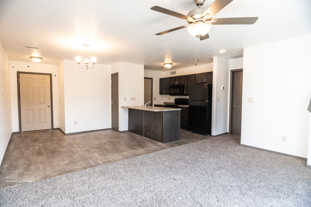 an empty living room with a kitchen and a ceiling fan