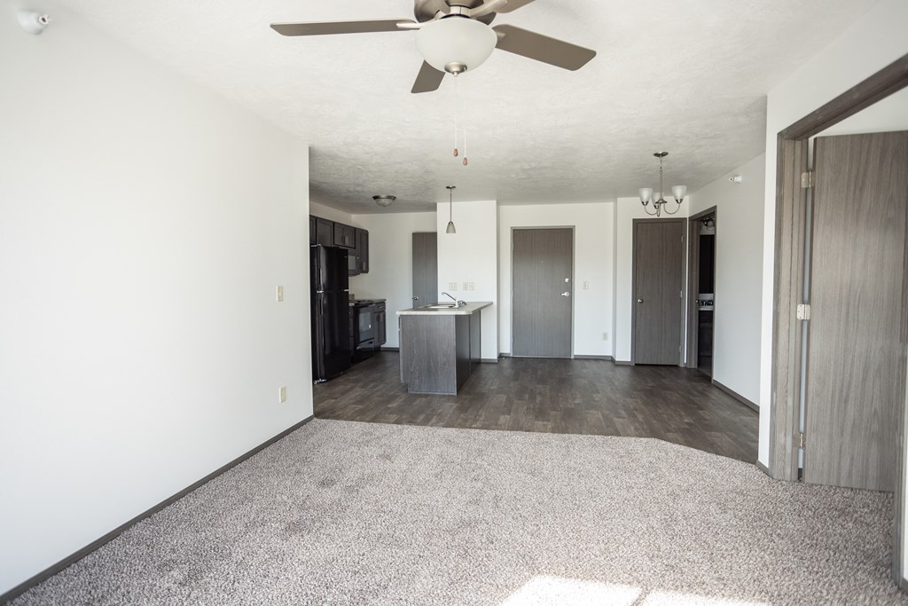 an empty living room with a ceiling fan and a kitchen