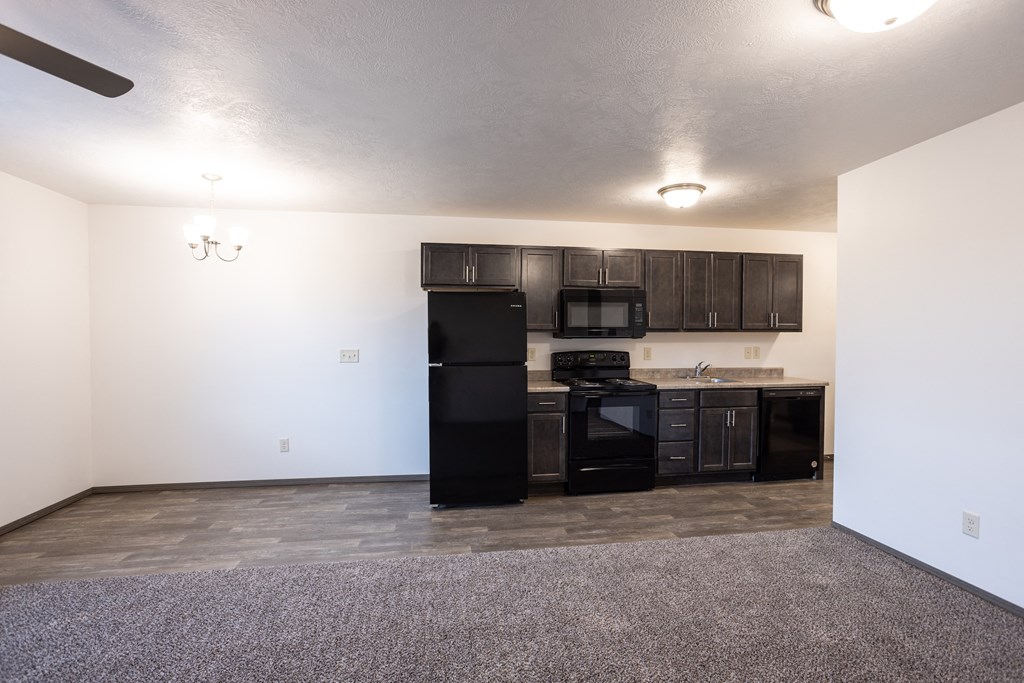 an empty living room with a kitchen with black appliances