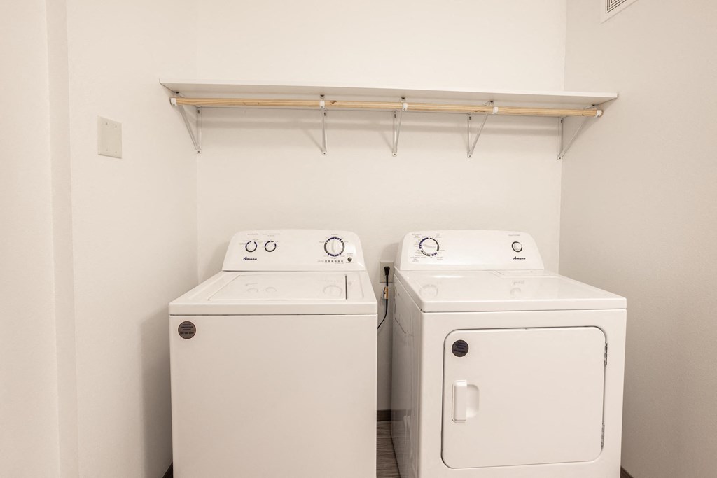 a washer and dryer in a white laundry room with a shelf above