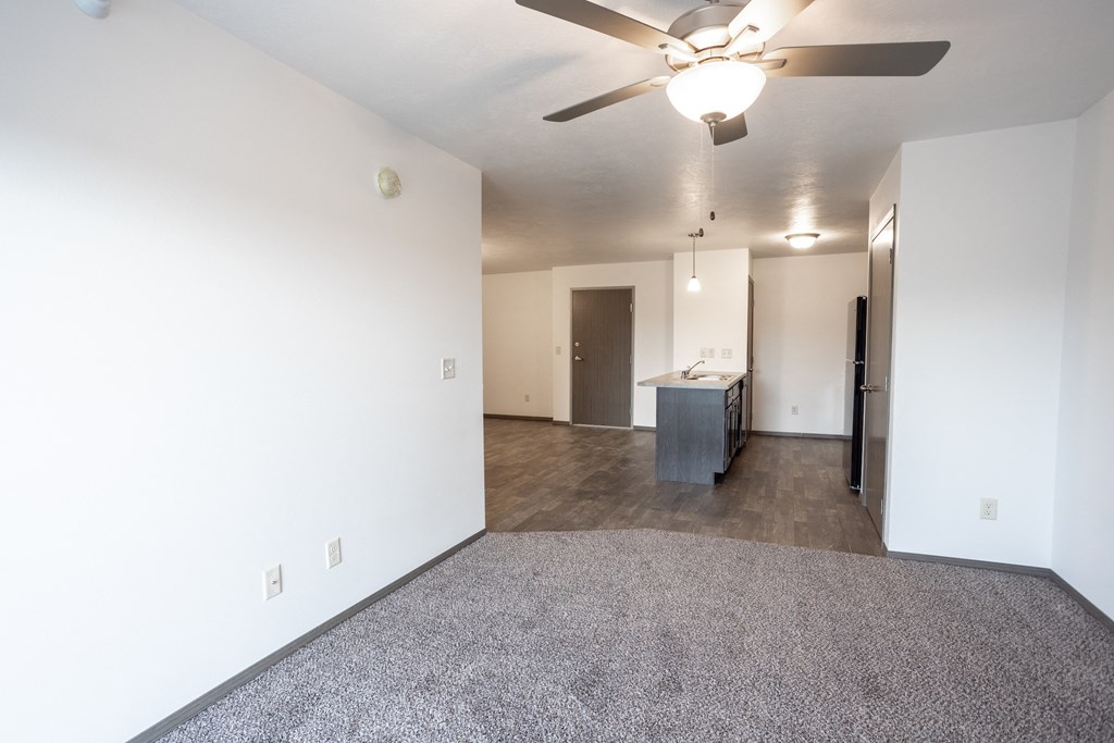 an empty living room with a ceiling fan and a kitchen