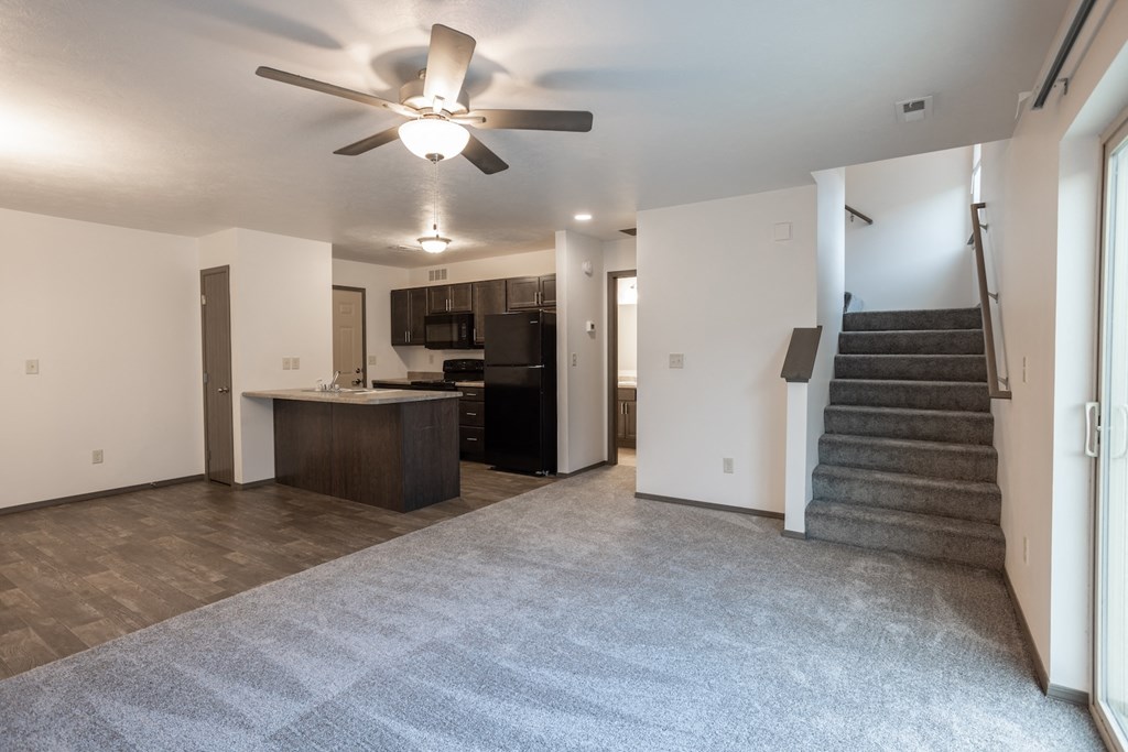 an empty living room with a ceiling fan and a staircase