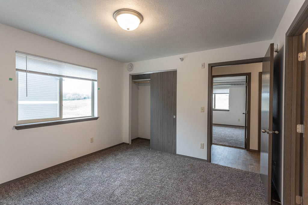 an empty living room with a large window and a door to a bedroom
