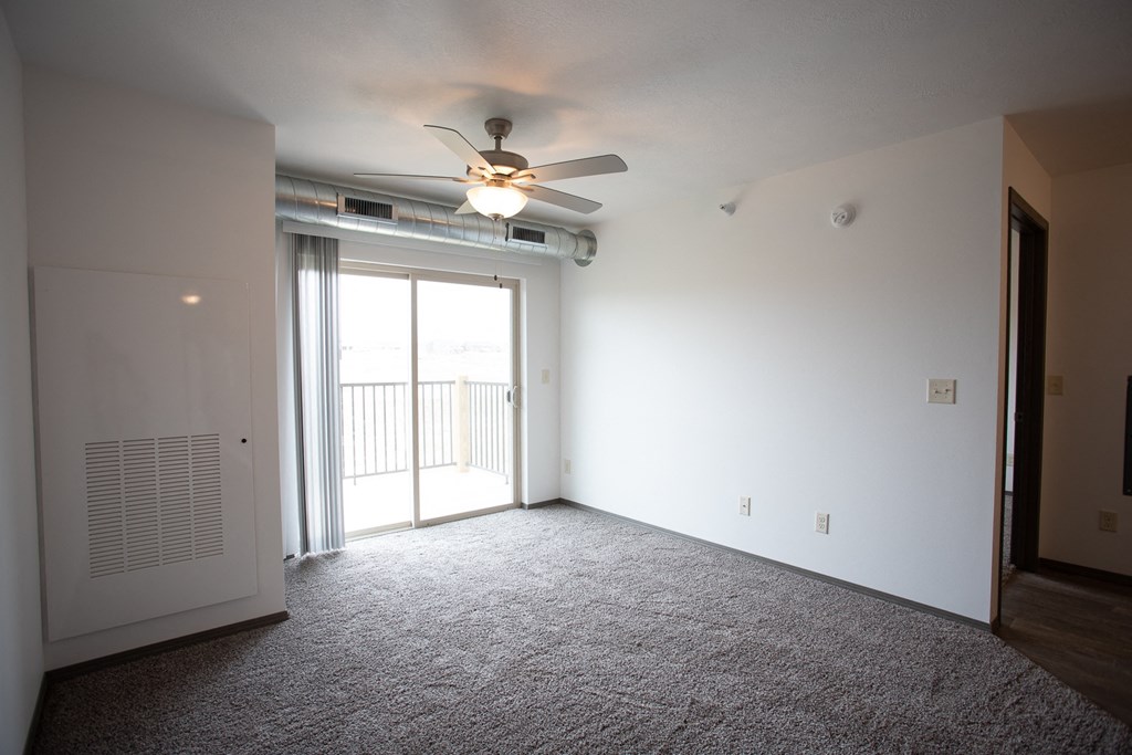 an empty living room with a ceiling fan and a door to a balcony