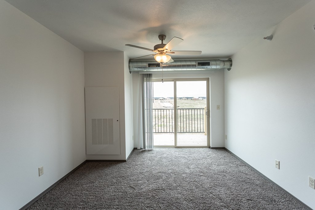 an empty living room with a ceiling fan and a door to a balcony
