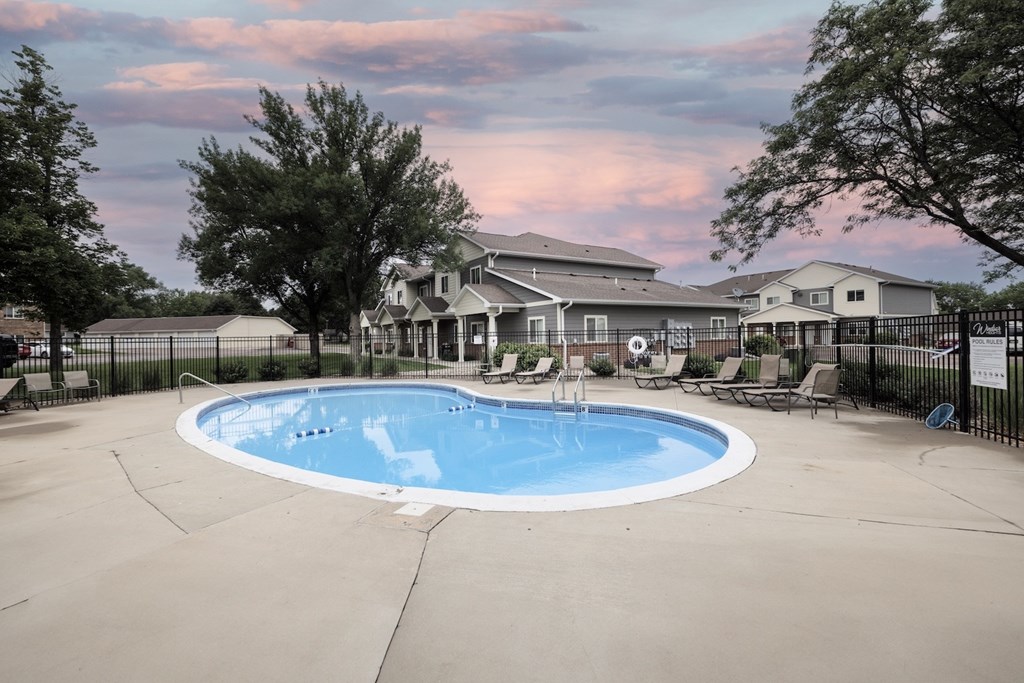 A large outdoor swimming pool surrounded by a fence and a house in the background.